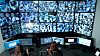 A female security operator wearing a headset monitors multiple surveillance camera feeds on large screens in a control room. She is focused on her workstation, communicating and analyzing real-time data to ensure safety and security. The scene highlights modern security systems, video surveillance technology, monitoring operations, and professional workplace environments in a high-tech setting.